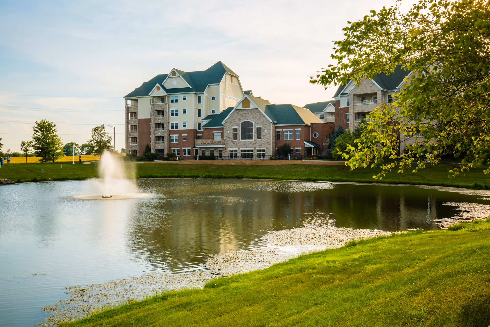 Smith Crossing senior living building beside a pond with a fountain and landscaped lawns.