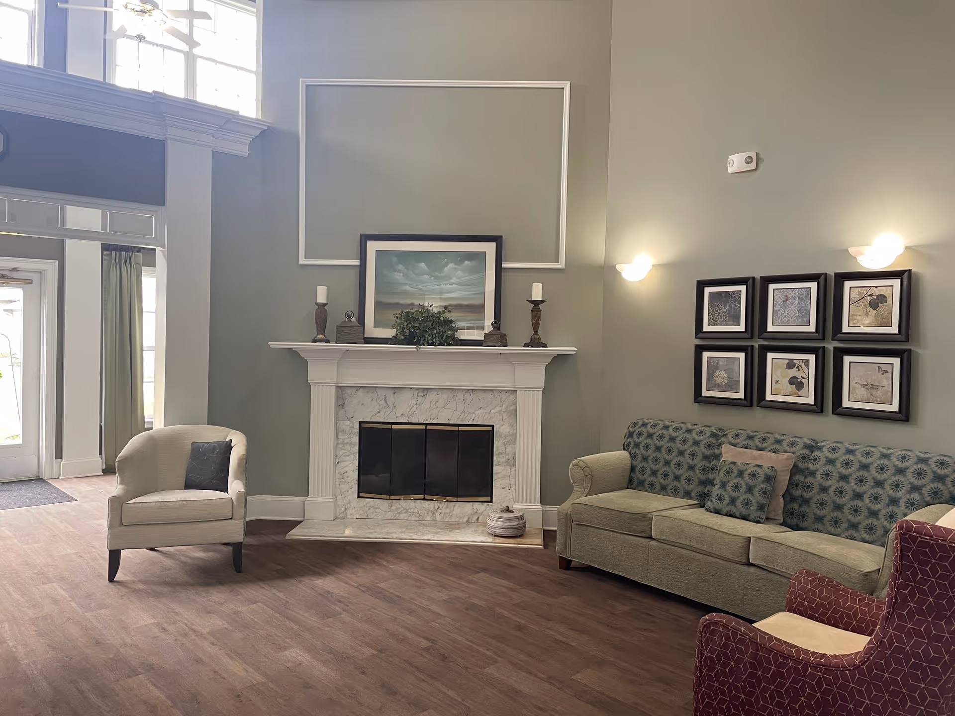 Spacious senior living lounge with a fireplace, framed artwork, and several upholstered chairs and a sofa.
