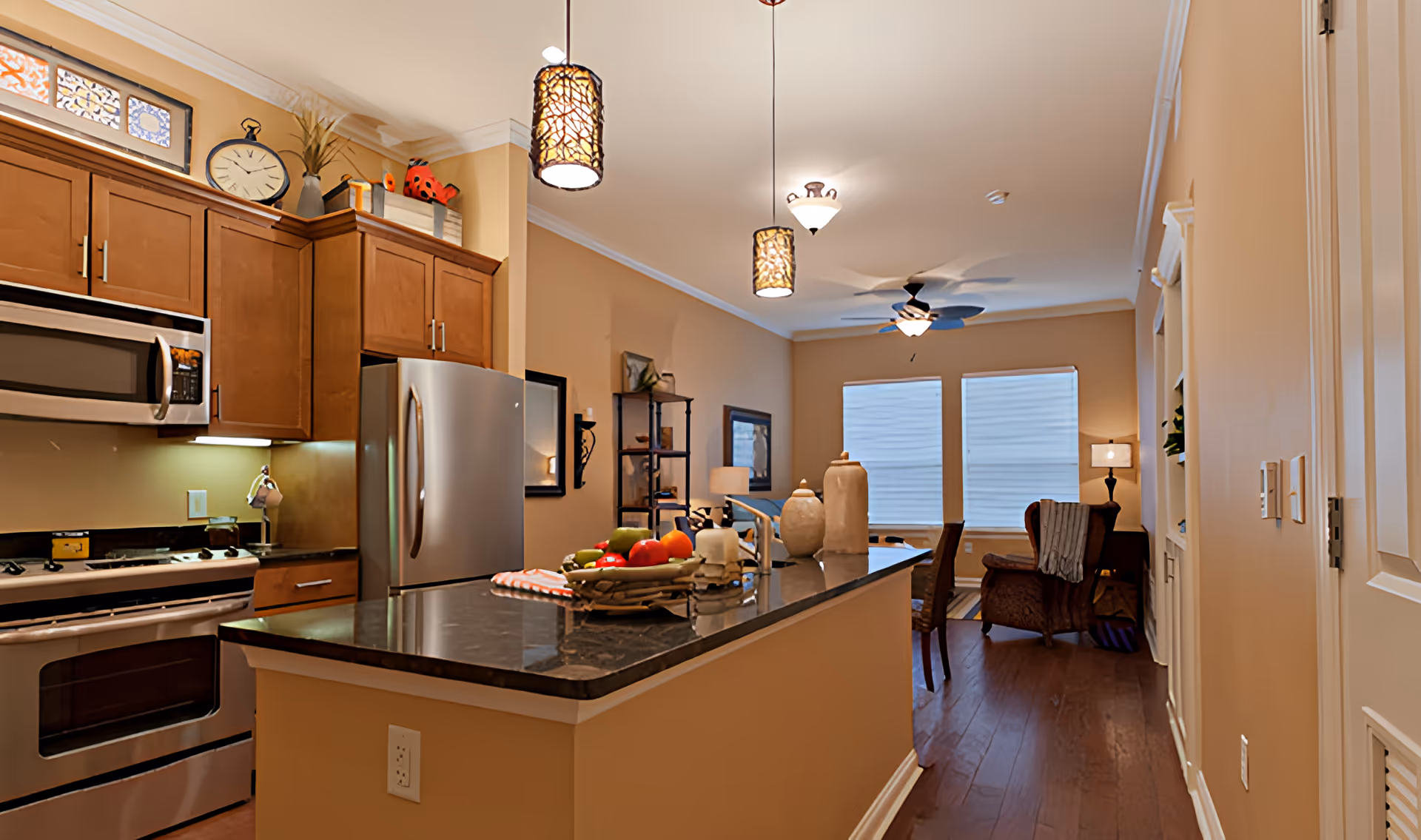 Open-concept kitchen with a central island, stainless steel appliances, pendant lights, and a view into a furnished living area.