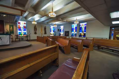 Chapel interior with wooden pews, stained-glass windows, and an altar.