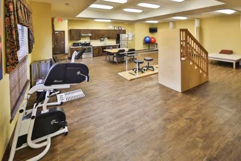 Bright senior living gym area with exercise equipment, mats, and a small kitchenette.