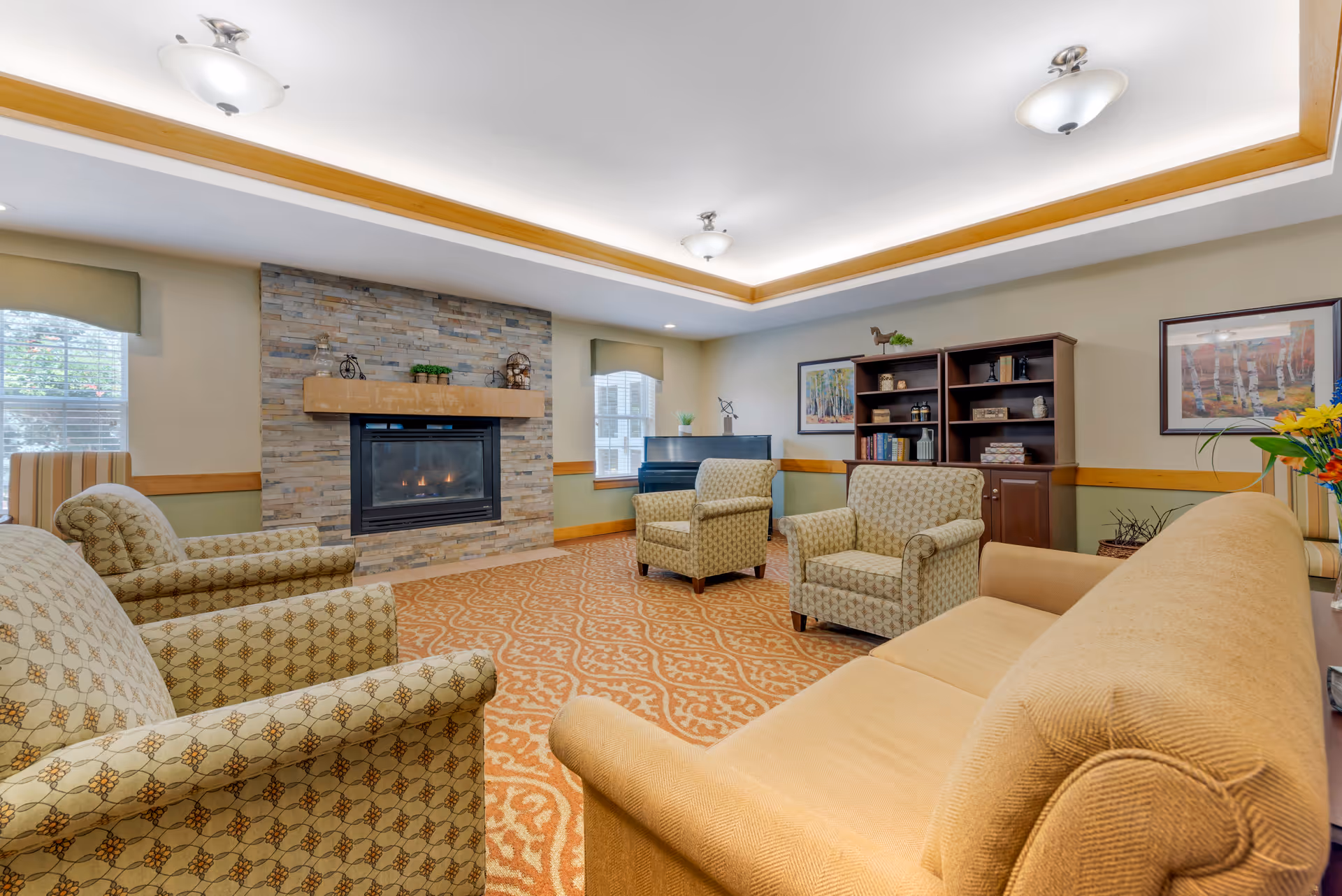 Comfortable communal lounge with upholstered chairs and a sofa arranged around a stone fireplace and bookshelf.