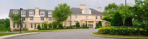 Cream-colored senior living center with arched windows, front entrance, and well-kept landscaping.