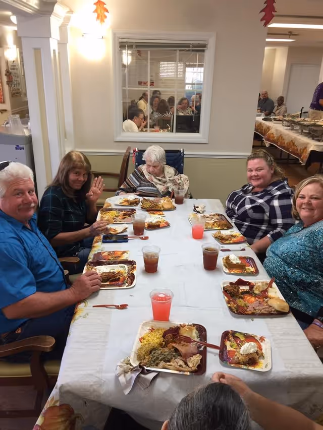 Several residents and visitors seated around a long table eating a meal in a communal dining room.