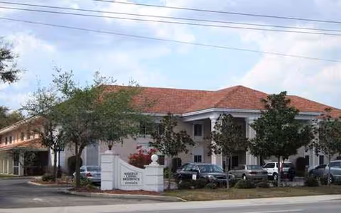 Front exterior of Savannah Grand of Sarasota with sign, trees, and parked cars along the curb.