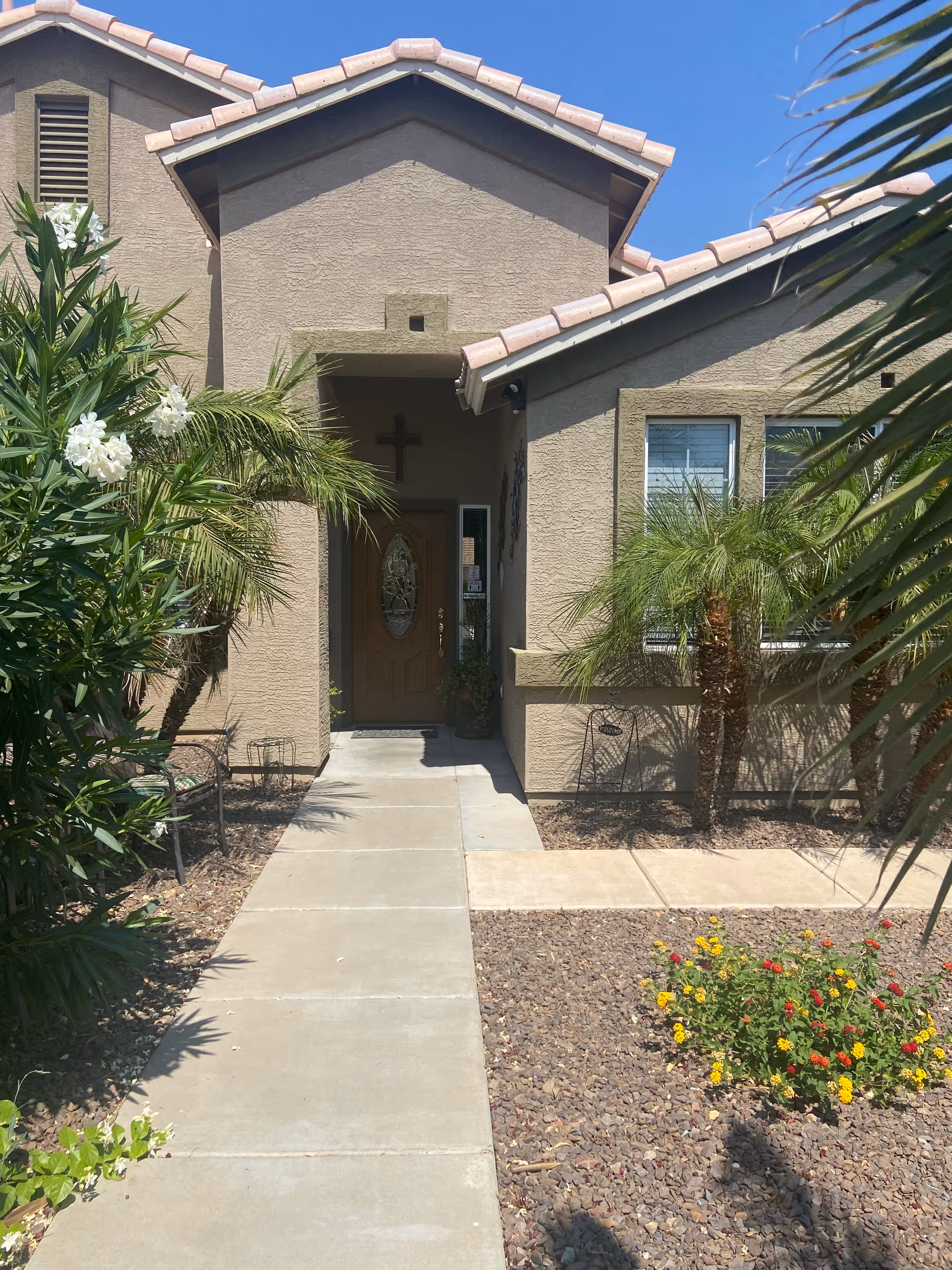 Walkway leading to the front entrance of a stucco house with a tiled roof, tropical landscaping, and an oval glass front door.