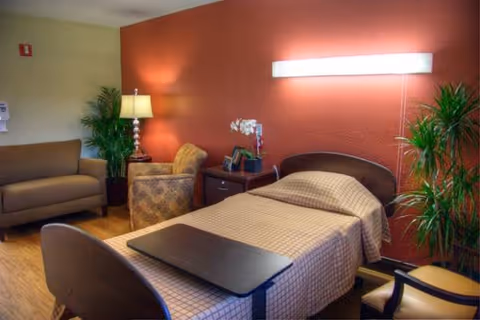 Senior living bedroom with a bed, seating area, plants, and warm lighting.
