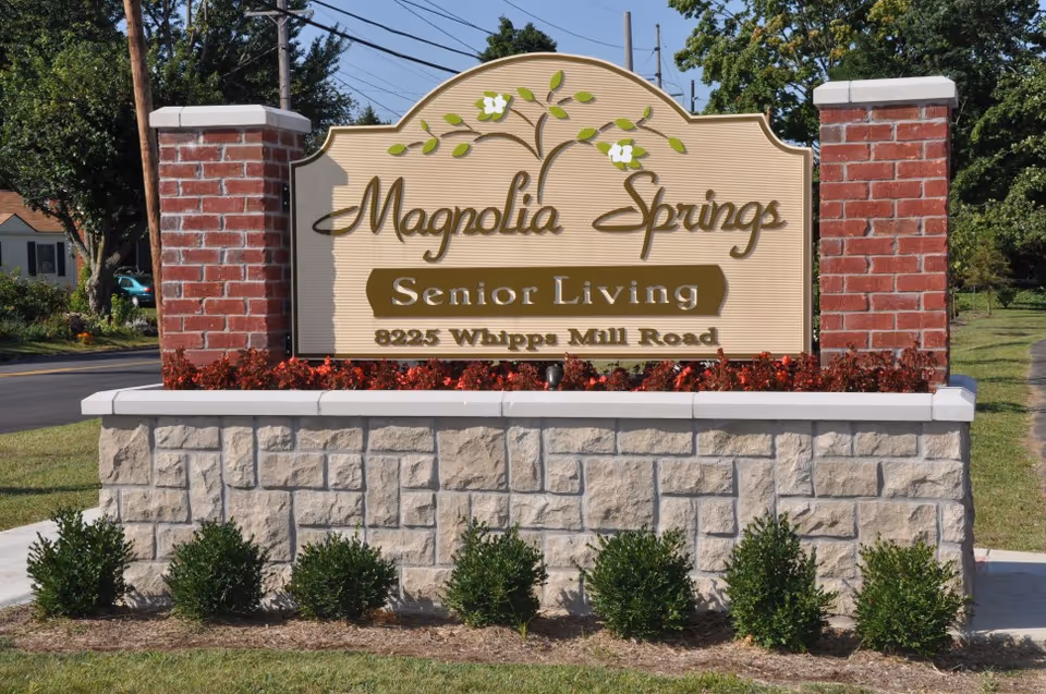 Stone and brick entrance sign reading "Magnolia Springs Senior Living, 8925 Whipps Mill Road" amid landscaping.