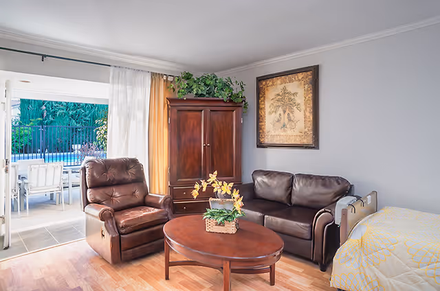 Cozy living room with a leather armchair and sofa, wooden coffee table and armoire, opening to a patio and pool.