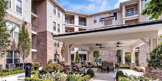 Courtyard patio with a covered seating area, tables and ceiling fans surrounded by landscaped gardens and a multi-story residential building.