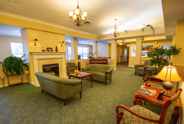 Communal lounge with patterned sofas and armchairs arranged around a fireplace and coffee tables under chandeliers.