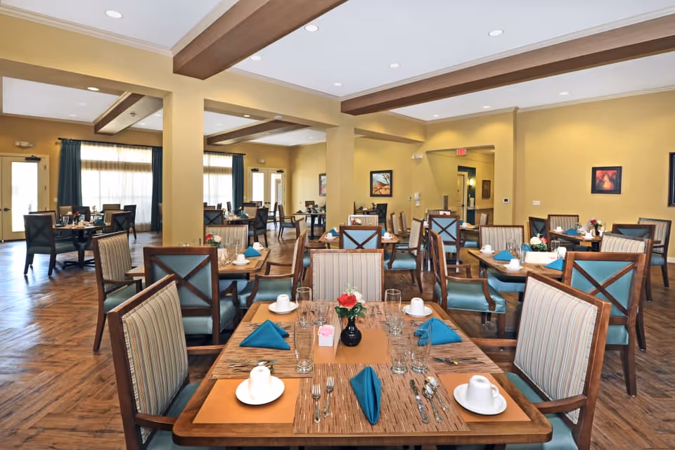 Large dining room with multiple set tables and chairs, teal napkins, and floral centerpieces.
