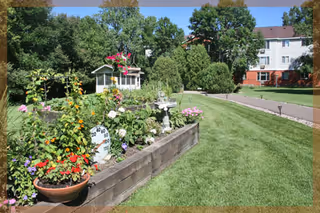 Well-maintained outdoor garden and lawn with flower beds, a gazebo and a multi-story building in the background.