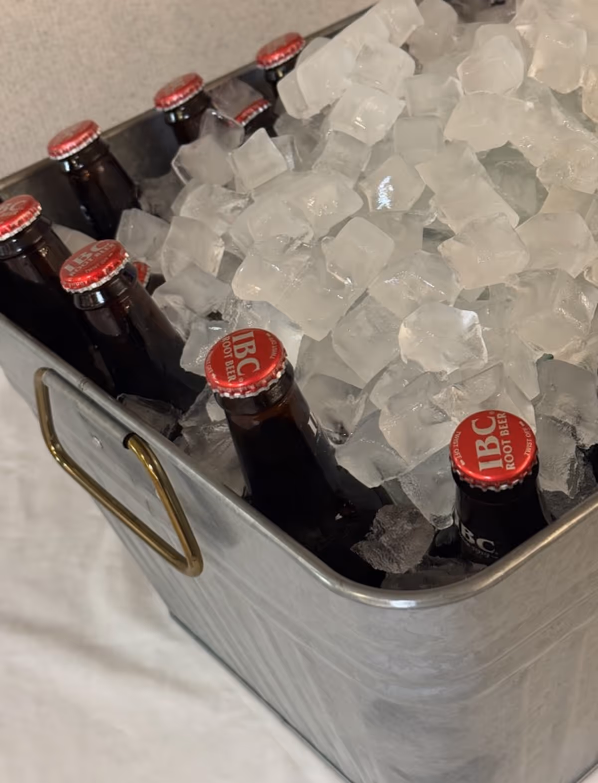 A galvanized metal tub filled with ice and several brown glass bottles topped with red IBC Root Beer caps.