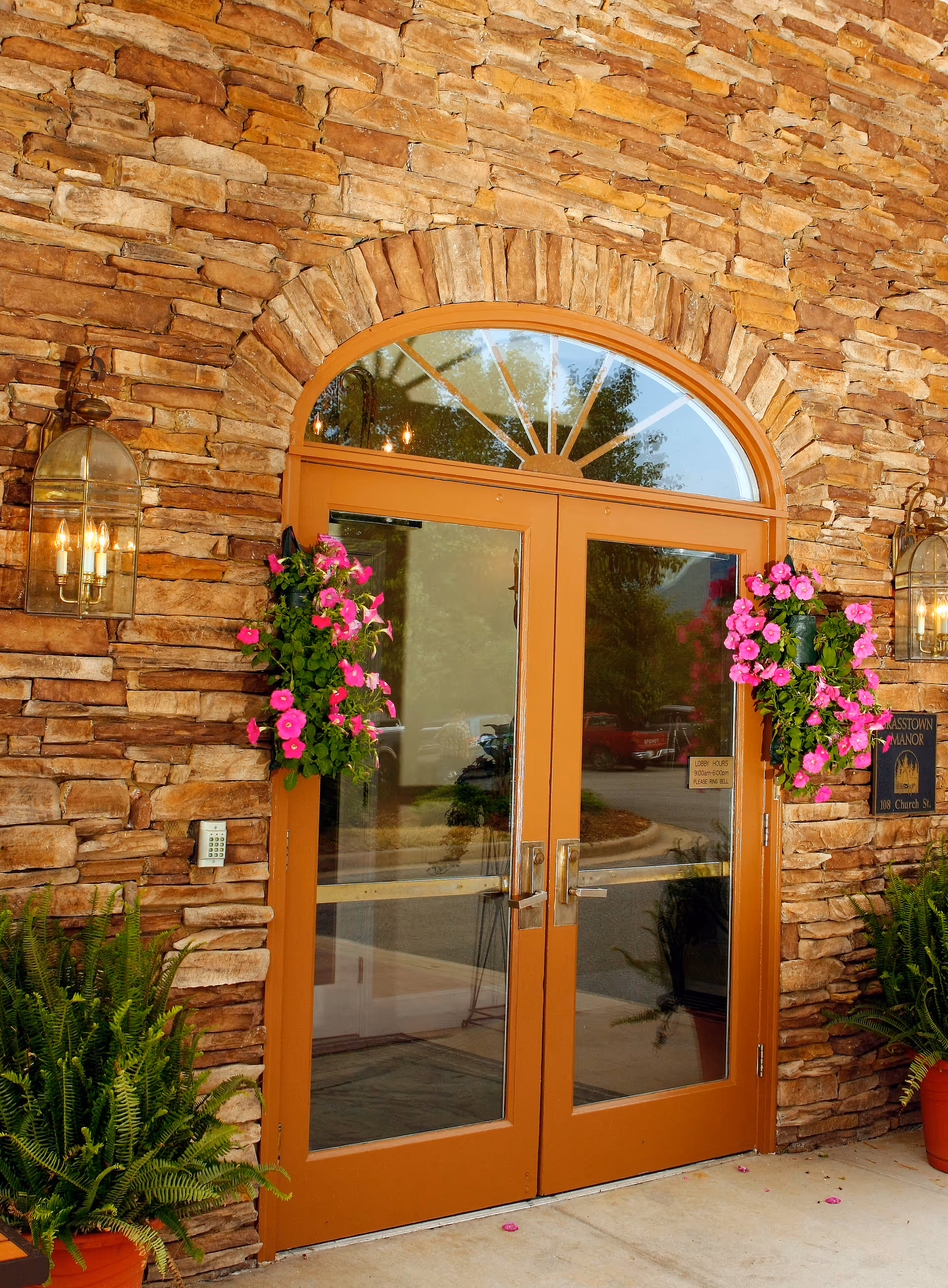 A welcoming entrance of Brasstown Manor Senior Living with stone walls, a large double door, and hanging flower pots.