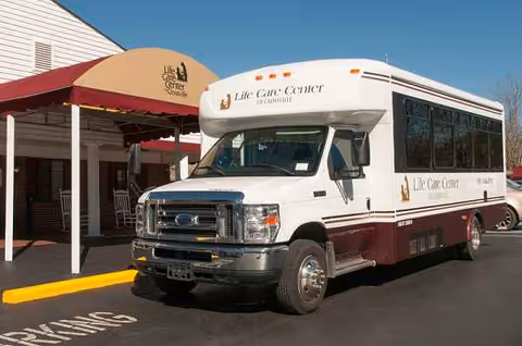 White Life Care Center shuttle bus parked in front of building entrance under a red awning.