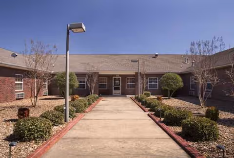 Brick exterior of Oak Manor Nursing Center with a walkway and landscaped entrance path.