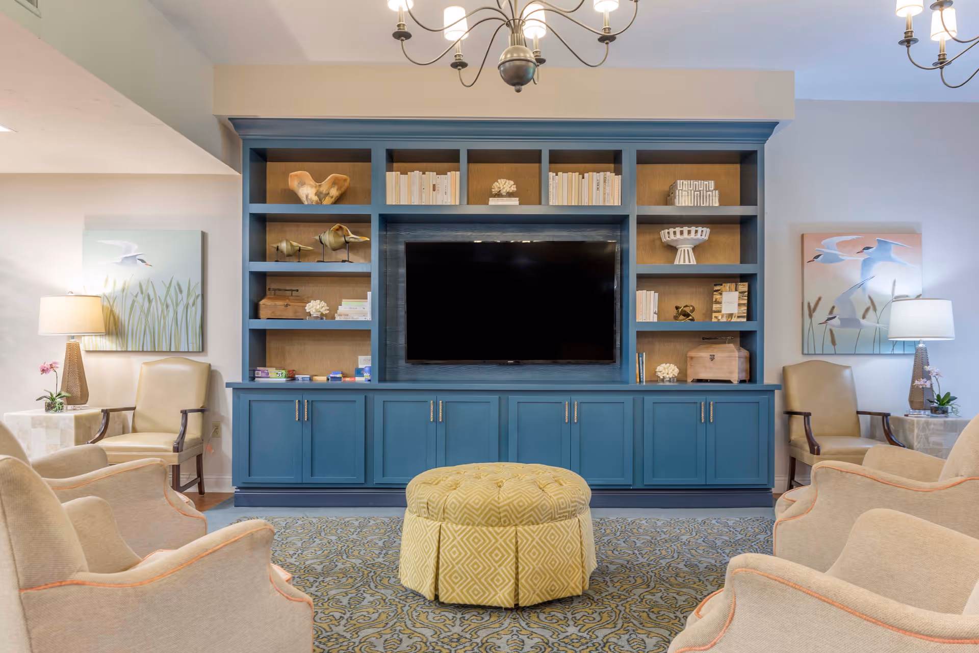 Cozy lounge featuring a blue built-in shelving unit with a central TV, surrounded by armchairs and soft lighting.