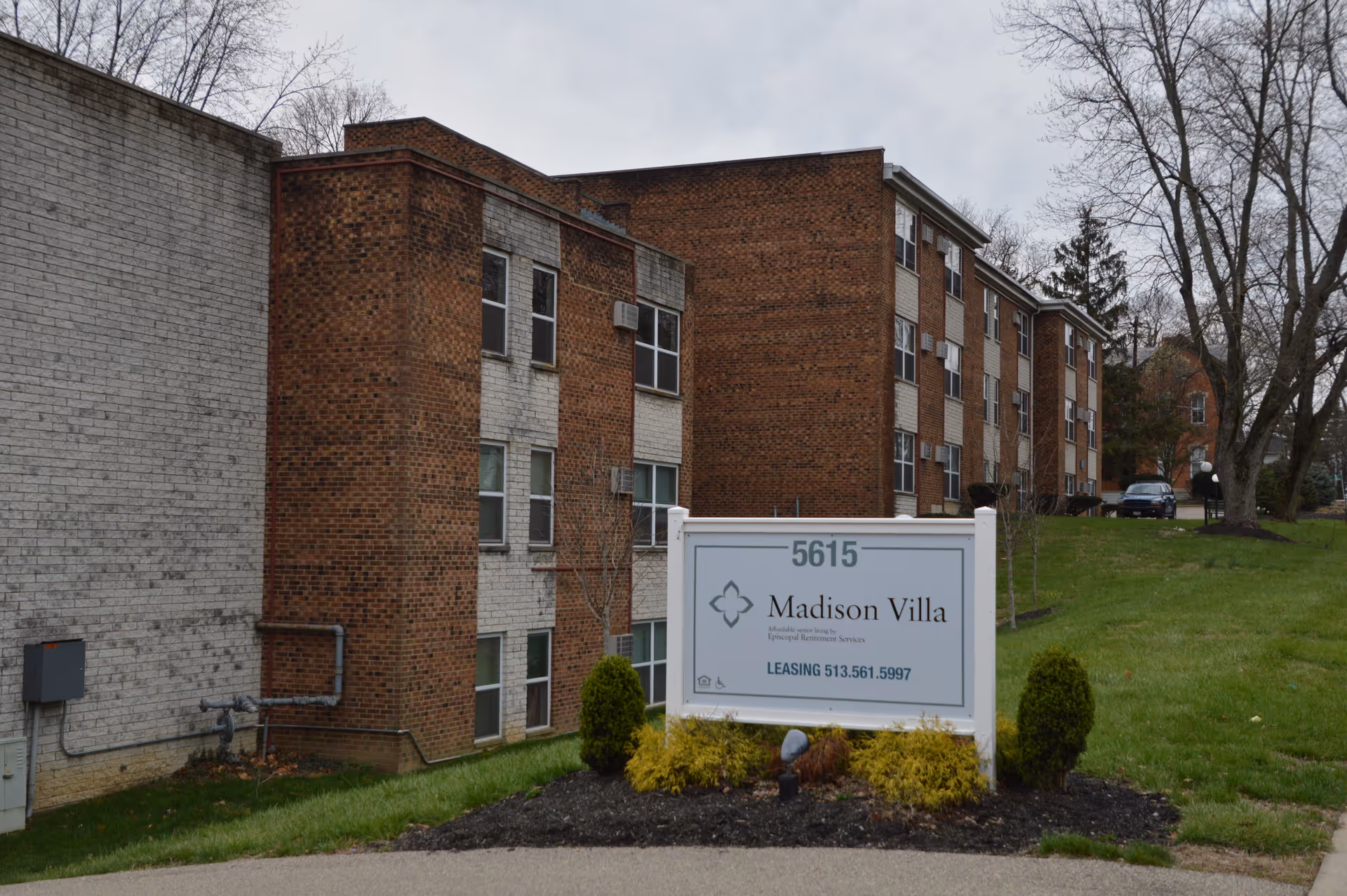 A brick multi-story apartment building with a white 'Madison Villa' sign and landscaped lawn in front.