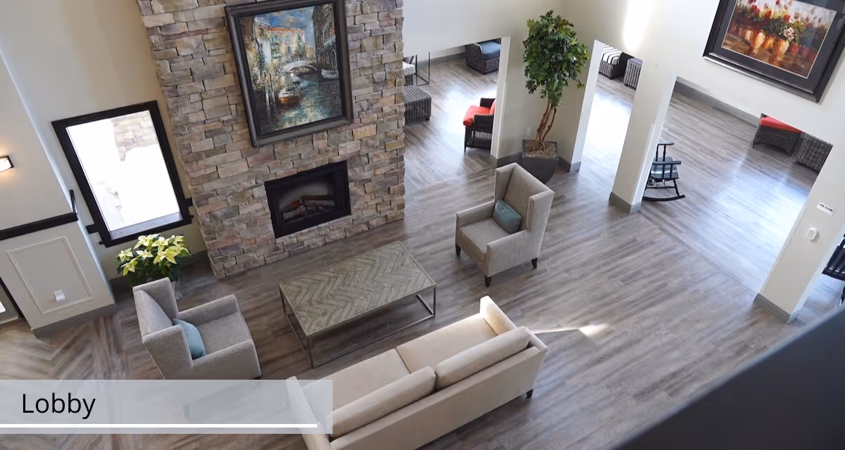 Aerial view of a bright senior living lobby with sofas, armchairs, a stone fireplace, artwork, and wood-look flooring.