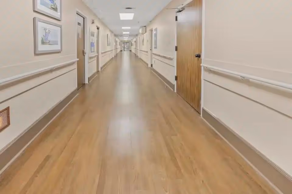 Long, well-lit hallway in a senior living facility with doors and handrails.