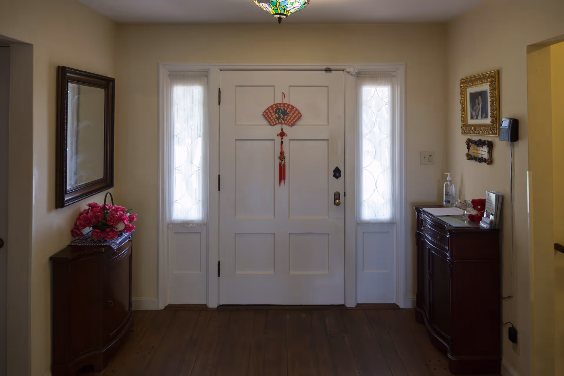 Front entry foyer with a white paneled door flanked by narrow windows and small wooden cabinets topped with decorations.