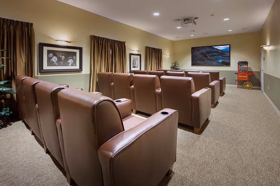 Small movie theater-style room with rows of brown leather recliner chairs facing a wall-mounted TV and a popcorn cart.