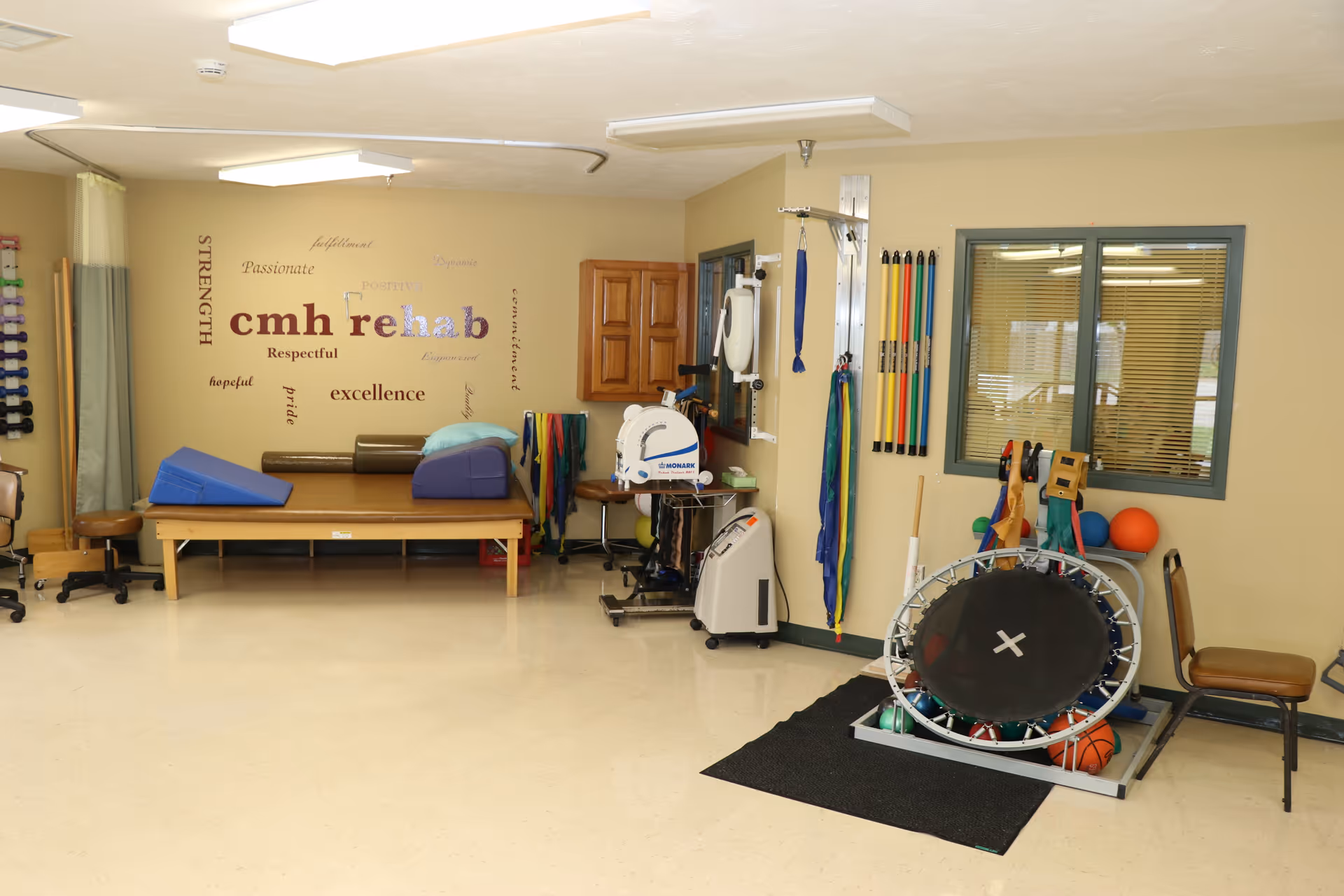 Indoor rehabilitation room with a therapy table, exercise equipment, and a wall displaying the words "cmh rehab."