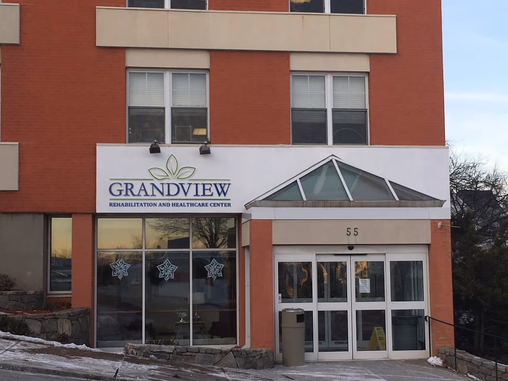 Front entrance of the Grandview Rehabilitation and Healthcare Center with glass doors, a sign, and the number 55 on a brick-and-stucco facade.