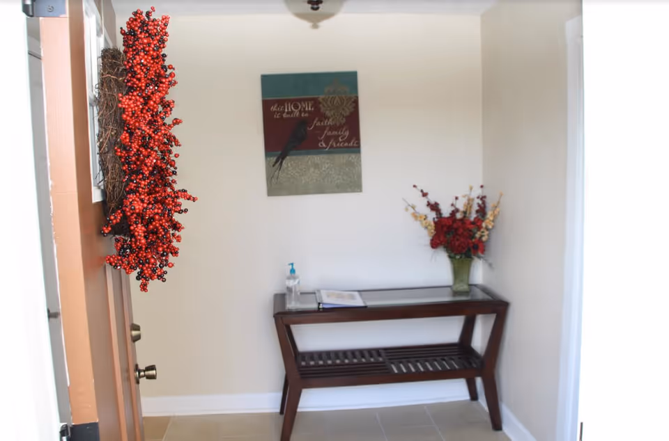 Small entry alcove near the door with a wooden console, wall art, and red floral arrangements.