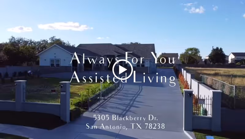 Front exterior view of Always For You Assisted Living Facility showing a driveway leading to a single-story building with a fenced yard on both sides under a clear blue sky.