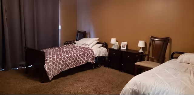 Shared bedroom with two twin beds, a central nightstand holding lamps and a small framed photo, brown walls and carpet.