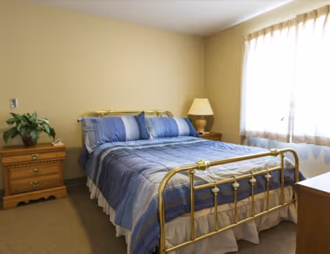 A tidy bedroom featuring a brass-framed bed with blue-striped bedding, wooden nightstands and a lamp by a curtained window.