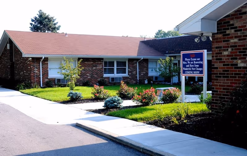 Single-story brick senior living building with landscaped front lawn, walkway, and a sign announcing renovations.