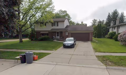 Front view of a two-story home-style senior living facility with a driveway and parked car.