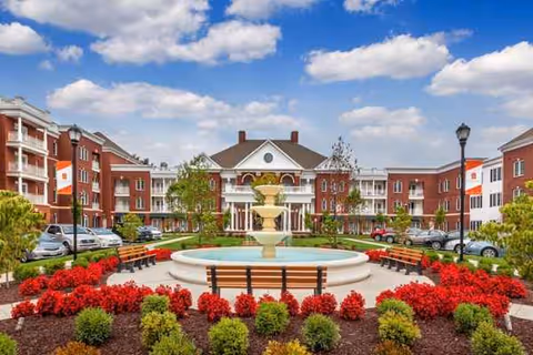 Front courtyard of The Village at Orchard Ridge with a central fountain and red flower beds.