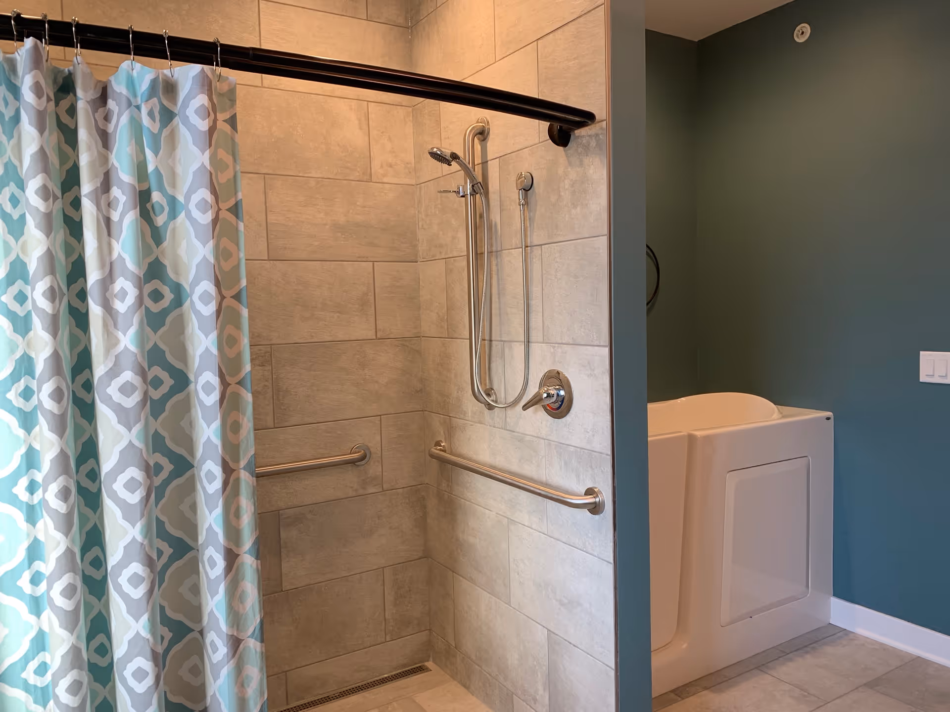 Tiled bathroom featuring a walk-in shower with grab bars, patterned shower curtain, and a walk-in bathtub.