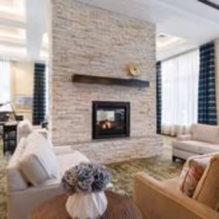 Cozy lounge with sofas and armchairs arranged around a stone fireplace and a small table with a floral arrangement.