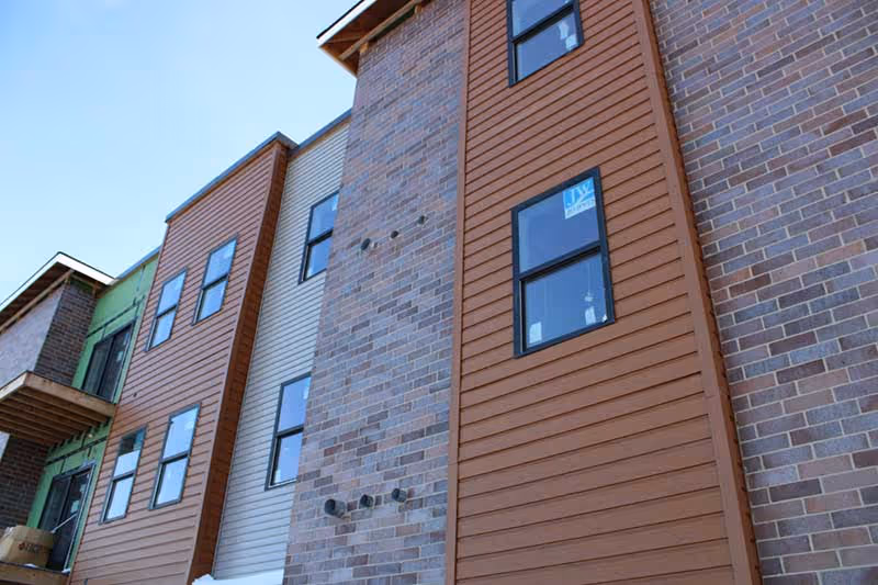 Exterior view of a multi-story building facade with brick and wood siding and several windows against a blue sky.