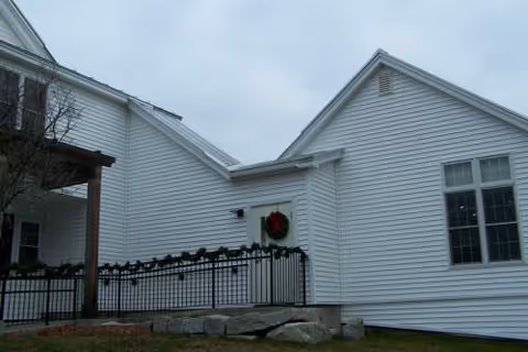White residential-style senior living facility exterior with railing and wreath at entrance.