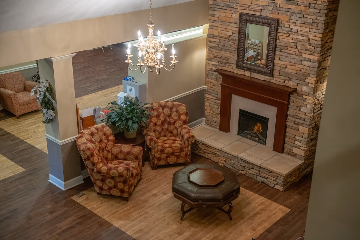 Cozy sitting area with patterned armchairs, a stone fireplace, chandelier, and octagonal coffee table.