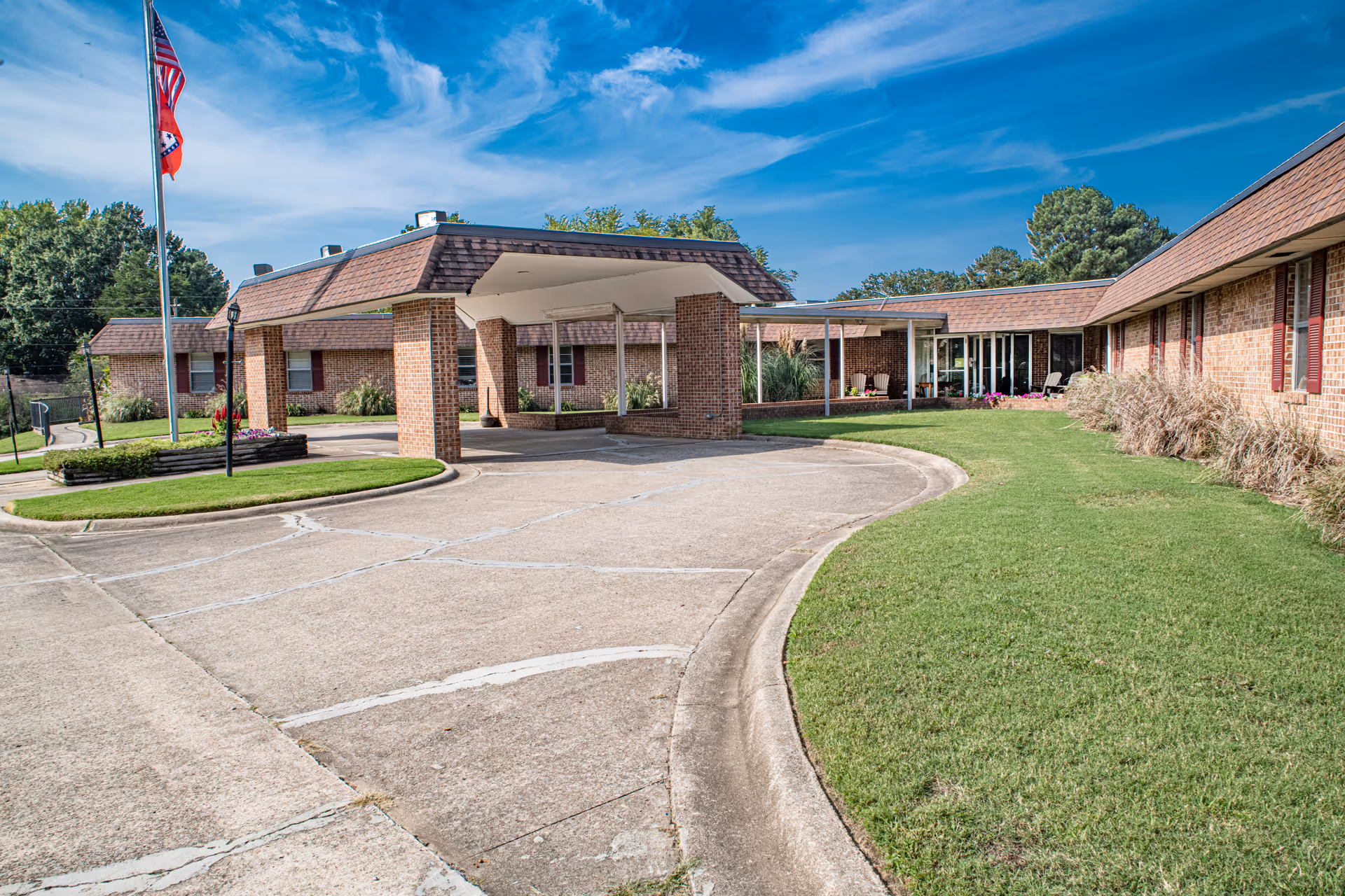 Front entrance of a low-rise brick health facility with a covered drop-off, flagpoles, and a curved driveway.