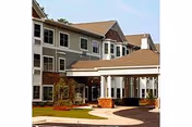 Exterior view of a multi-story senior living facility building with a covered entrance, landscaped grounds, and a paved driveway.