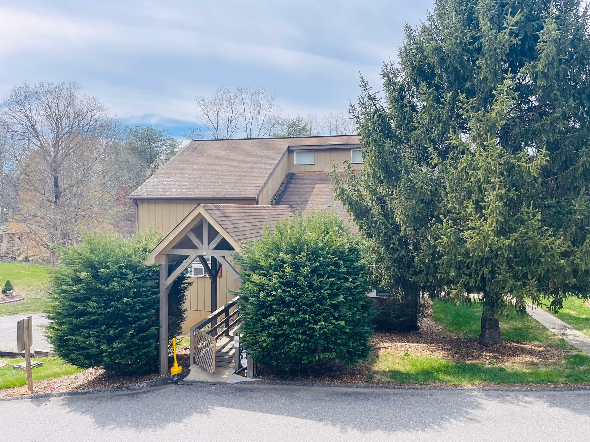 Exterior view of a building at Richmond Hill with a wooden covered entrance ramp surrounded by green bushes and trees, under a partly cloudy sky.