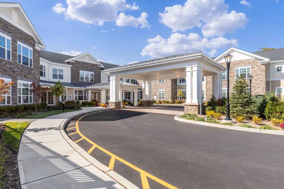 Front entrance of Sunrise of Franklin Lakes with a covered porte-cochère, curved driveway, and landscaped grounds.