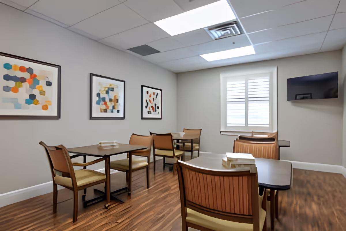 Small dining room with several tables and chairs, abstract wall art, a window with shutters, and a wall-mounted TV.