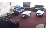 Common lounge area with several black leather sofas, coffee tables, a TV, and a side lamp.