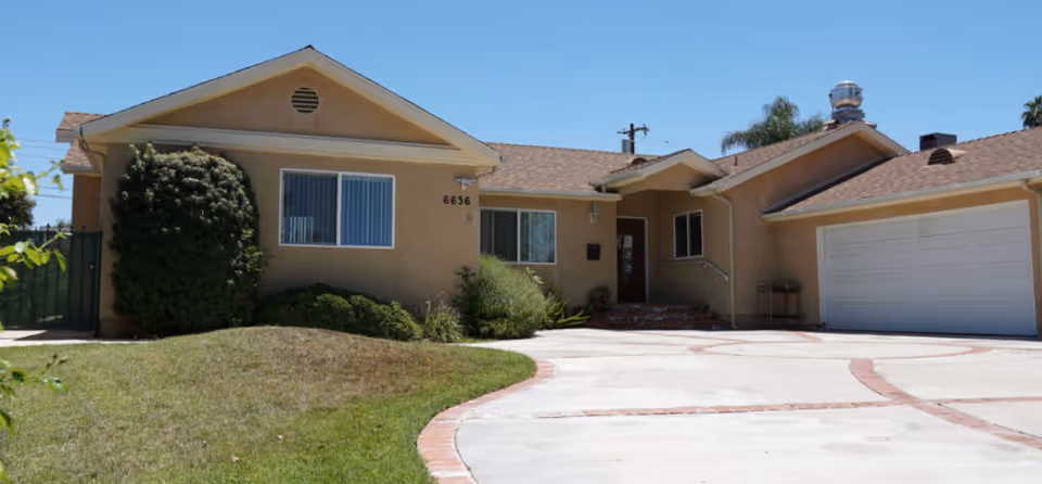 Front view of a single-story beige house with a curved driveway and a two-car garage.