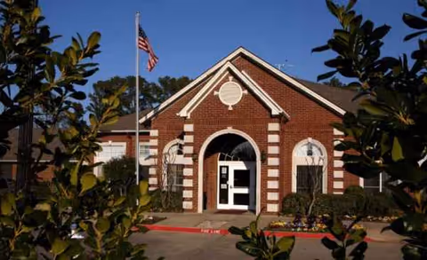Brick building with arched entrance, American flag, and shrubbery framing the front.