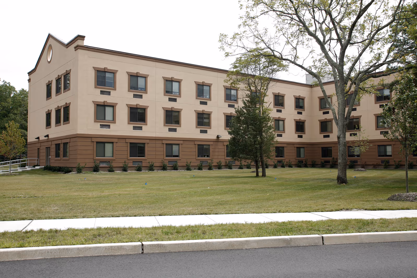 A multi-story beige senior living facility with a manicured lawn and trees.
